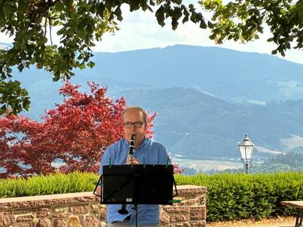 Quelle: Markus Weber Ein Mann spielt draußen Klarinette, im Hintergrund Aussicht auf Bäume und eine Dorfkirche im Schwarzwald.